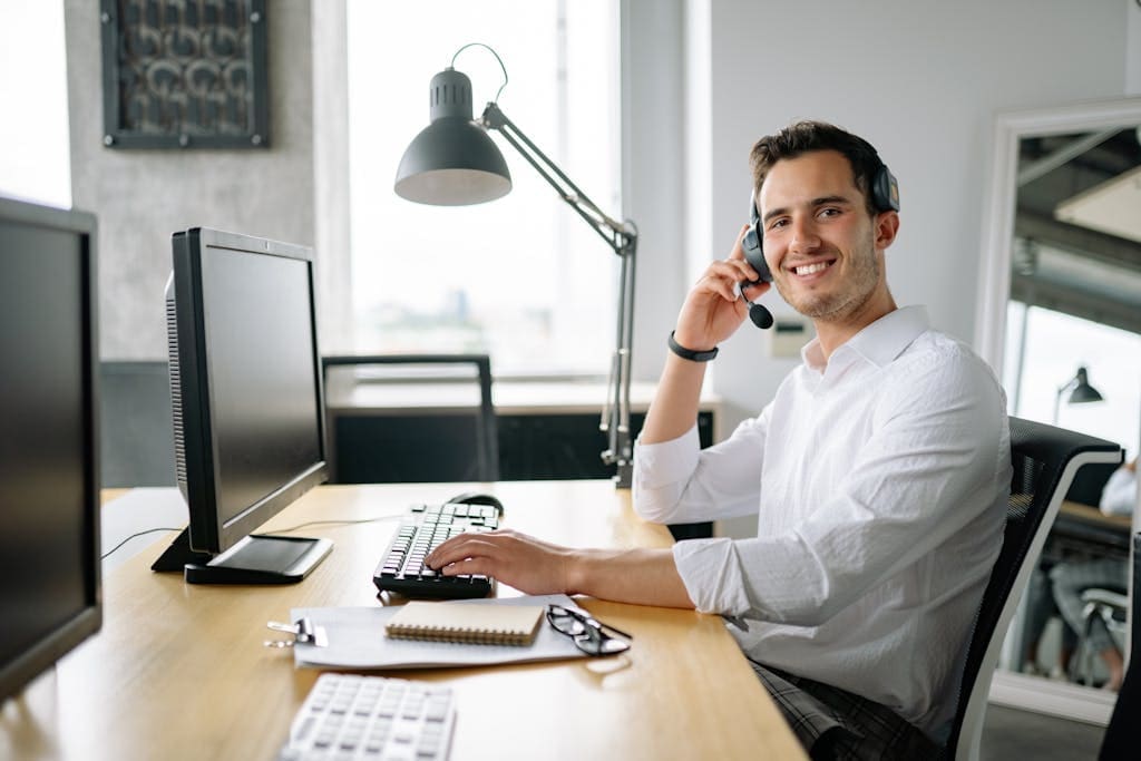 Smiling business owner talking remotely with their bookkeeper at a desk with a headset and computer in a modern office.