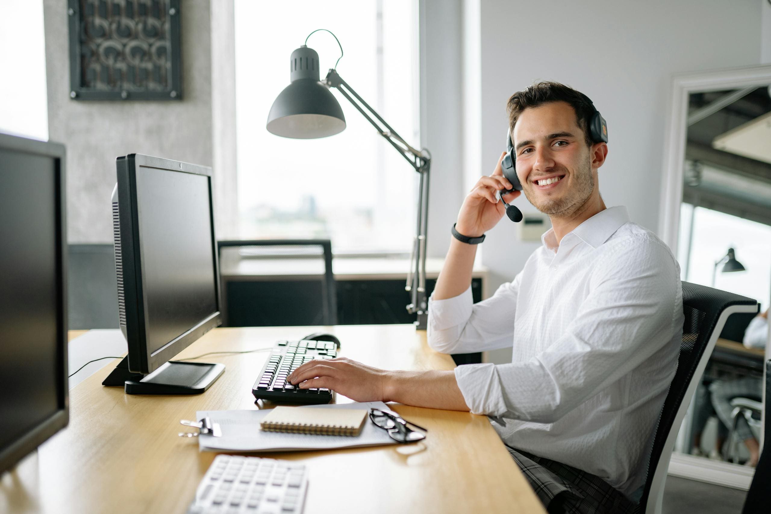 Smiling business owner talking remotely with their bookkeeper at a desk with a headset and computer in a modern office.