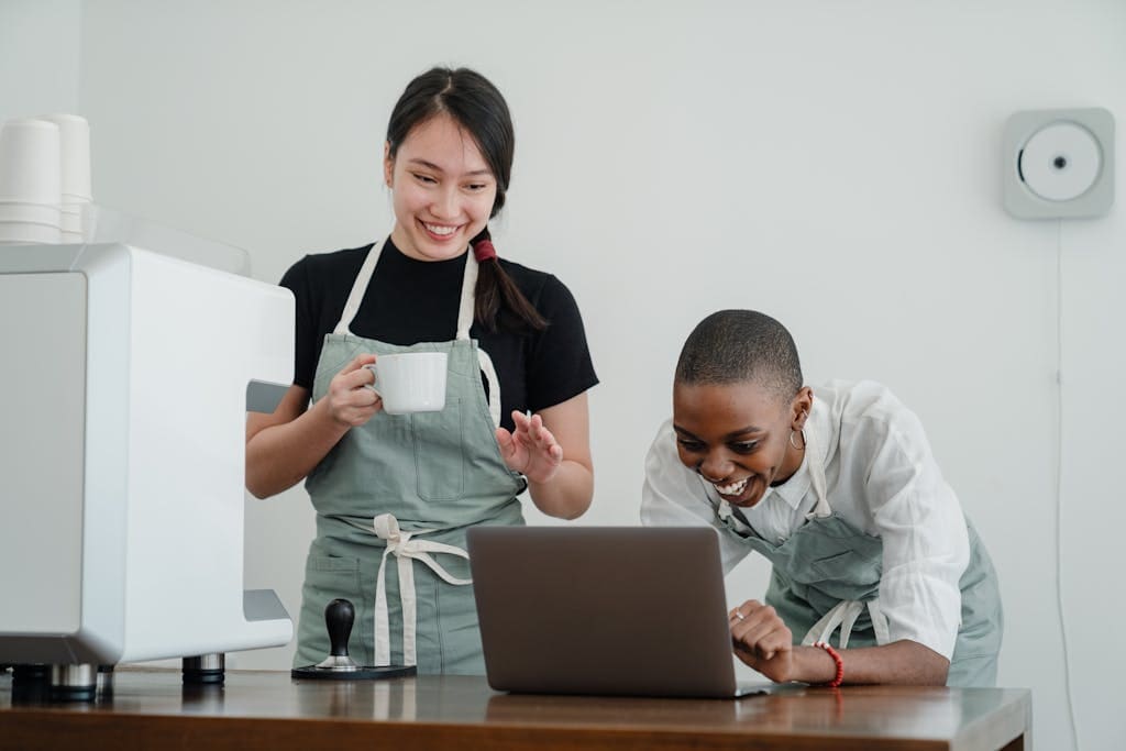 Two baristas enjoying work, actively collaborating and smiling together in a coffee shop.