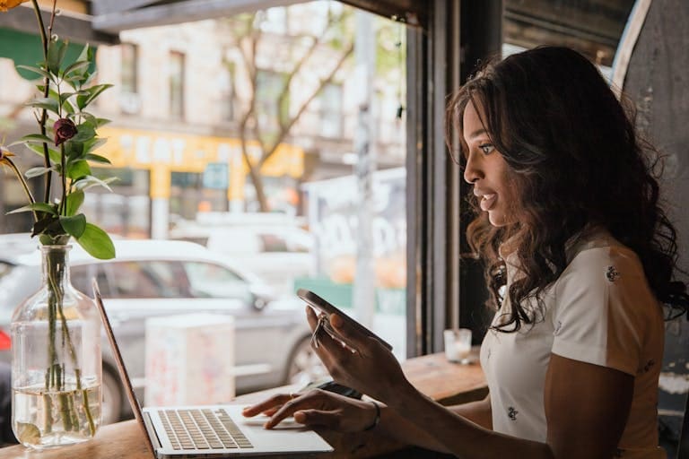 Afro American female business owner working on laptop and phone in urban café setting.
