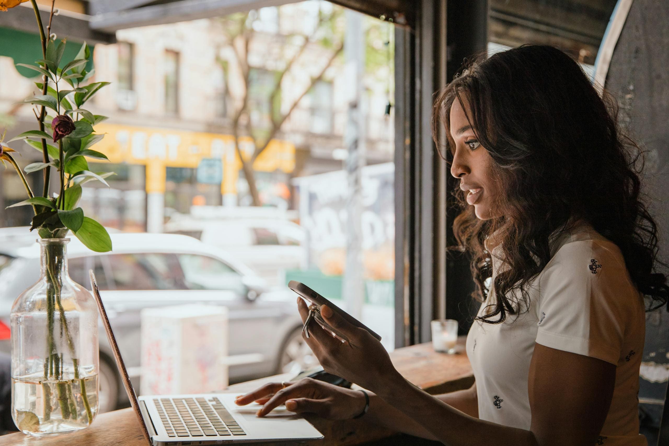 Afro American female business owner working on laptop and phone in urban café setting.